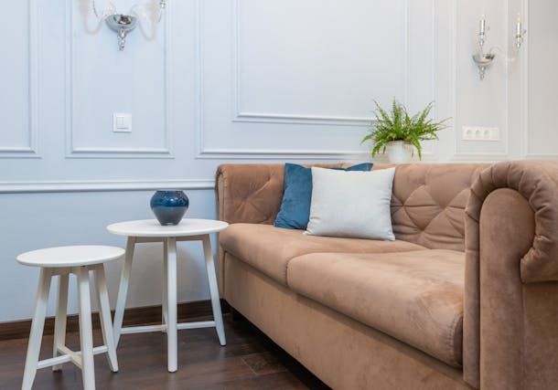 a brown couch and with white and blue pillows and a round side table